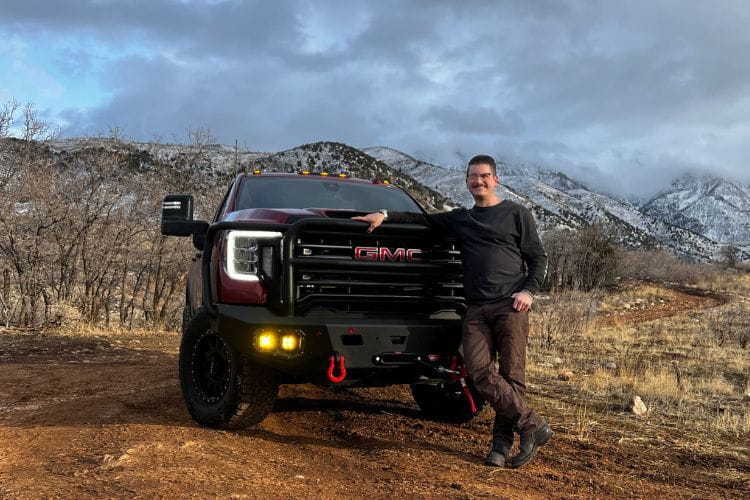 GMC truck with heavy duty off road bumper and winch parked on a mountain trail, with a man standing beside the truck.