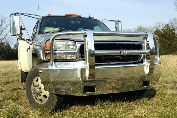 Ali Arc Sentinel front bumper GMC Sierra 2500 3500 HD 2003-2006 chrome grille guard front view installed in an open field with trees in the background