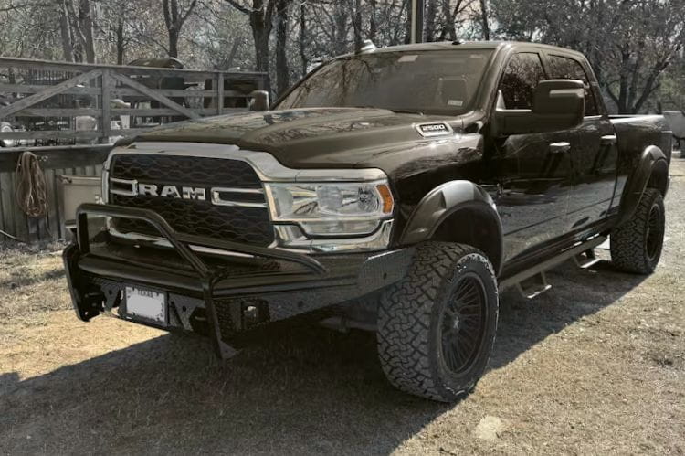 Fab Fours Black Steel Pre-Runner Guard front bumper for 2019–2024 Dodge Ram 2500 and 3500 HD (new body style), heavy-duty off-road steel bumper with integrated grille guard parked on a dirt road with trees in the background