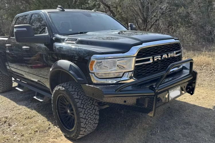 Fab Fours Black Steel Pre-Runner Guard front bumper for 2019–2024 Dodge Ram 2500 and 3500 HD (new body style), heavy-duty off-road steel bumper with integrated grille guard with trees in the background