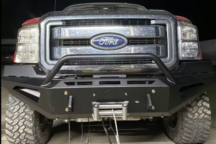 Front view of a black powder-coated Fab Fours Red Steel front bumper featuring a pre-runner hoop guard and winch mount, installed on a 2011-2016 Ford Super Duty truck.