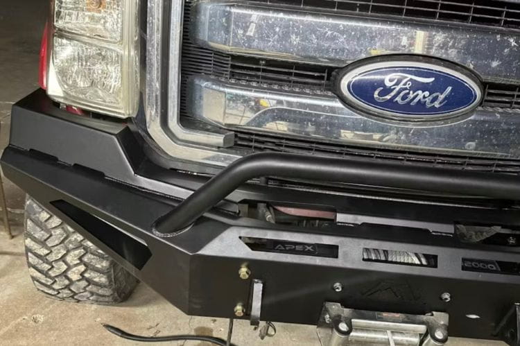 Black powder-coated Fab Fours Red Steel front bumper featuring a pre-runner hoop guard and winch mount, installed on a 2011-2016 Ford Super Duty truck.