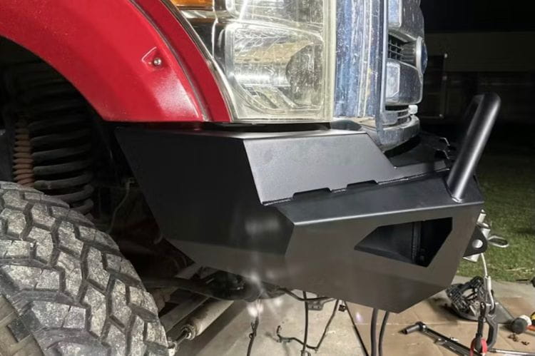 Side-view of a black powder-coated Fab Fours Red Steel front bumper featuring a pre-runner hoop guard and winch mount, installed on a 2011-2016 Ford Super Duty truck.