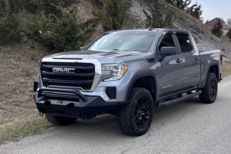 Fab Fours GS19-X3952-1 Matrix Series Front Bumper with Pre-Runner Guard for 2019-2022 GMC Sierra 1500, Winch Ready Slim Steel Bumper on a road with trees and rocks in the background