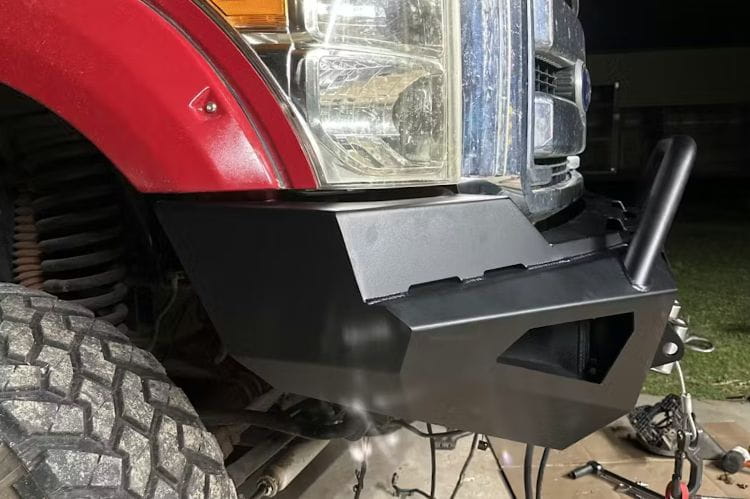 Close-up of a Fab Fours Red Steel FS17-RS4162-1 front bumper on 2017-2022 Ford F250 F350 Super Duty winch ready pre-runner guard in grassy area in the background.
