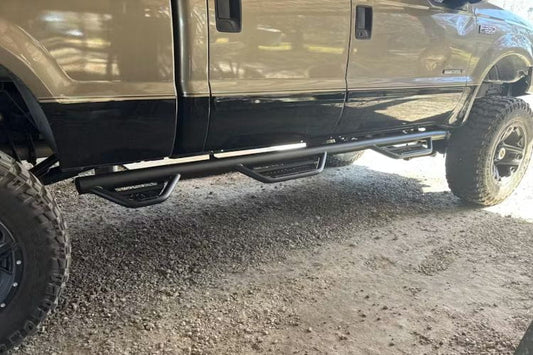 Side view of a vehicle with N-Fab HPF99105CC-6-TX Podium LG stainless steel steps bar for 1999–2016 Ford F250 and F350 Super Duty Crew Cab with single rear wheel and 6'9" bed, durable side step with textured step pads on a gravel surface