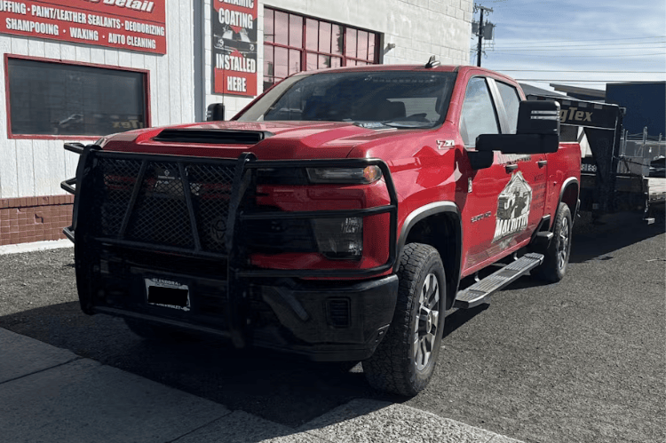 Red pickup truck with Ranch Hand Legend Series Grille Guard GGC241BL1 installed on a 2024-2026 Chevy Silverado 2500HD 3500HD diesel truck parked in front of a building.