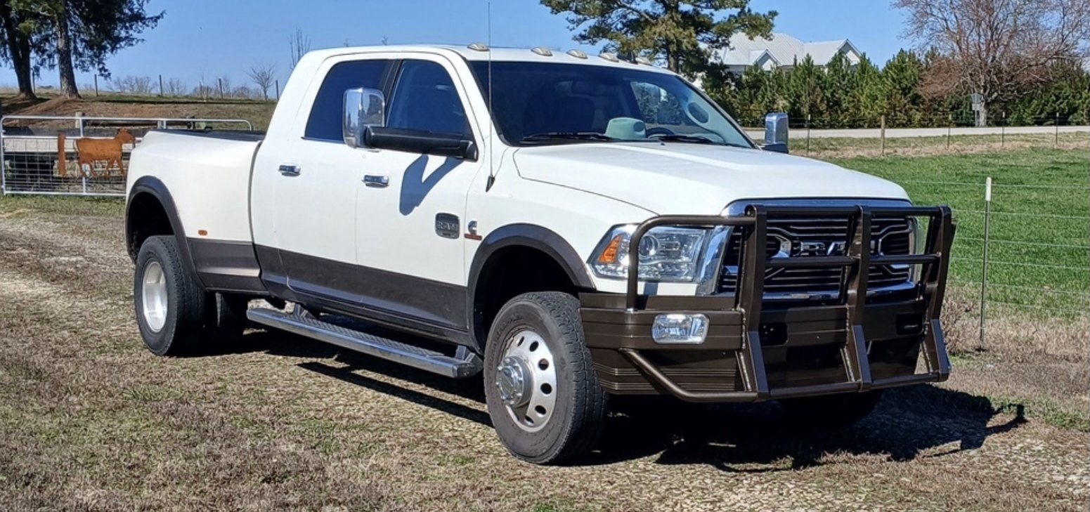 A white Ram 3500 dually with an Ali Arc Classic front bumper, parked by a pasture fence