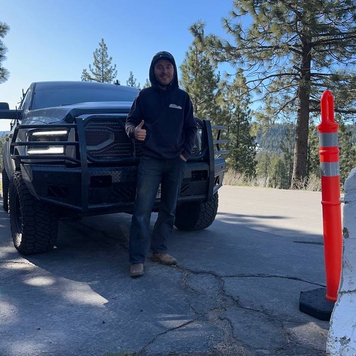 A customer giving a thumbs up next to his Ram with a grille guard, mountains behind