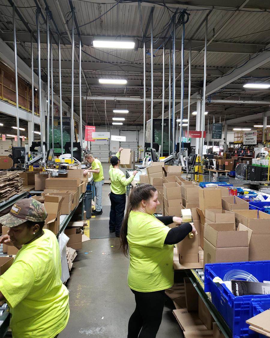 Workers packing orders at a distribution warehouse, boxes on a roller conveyor
